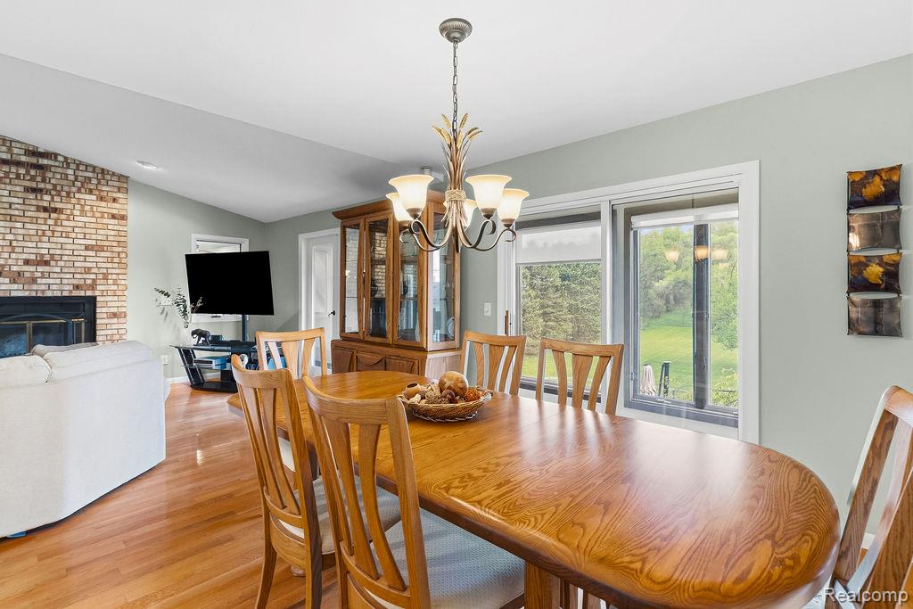 8742 Hyne Road Brighton, MI 48114 - Photo 17 of 65 Dining area featuring lofted ceiling, light wood-style flooring, hanging lights, and a brick fireplace