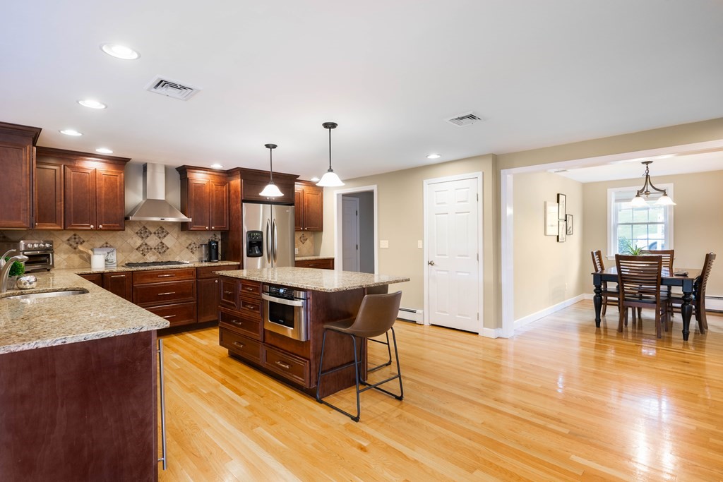 6 Old Meadow Lane Canton, MA 02021 - Photo 5 of 35 a kitchen with stainless steel appliances granite countertop a stove a refrigerator a sink a dining table and chairs with wooden floor