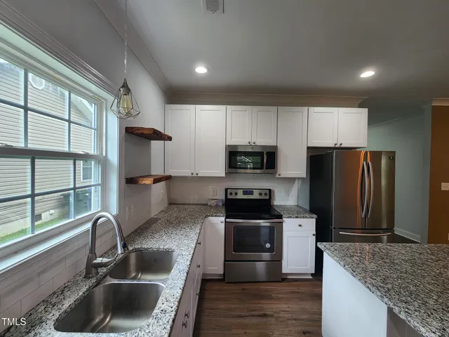a kitchen with granite countertop a sink wooden floor and stainless steel appliances