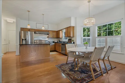 a open kitchen with stainless steel appliances granite countertop a stove top oven a dining table and chairs with wooden floor