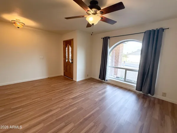 an empty room with wooden floor fan and windows
