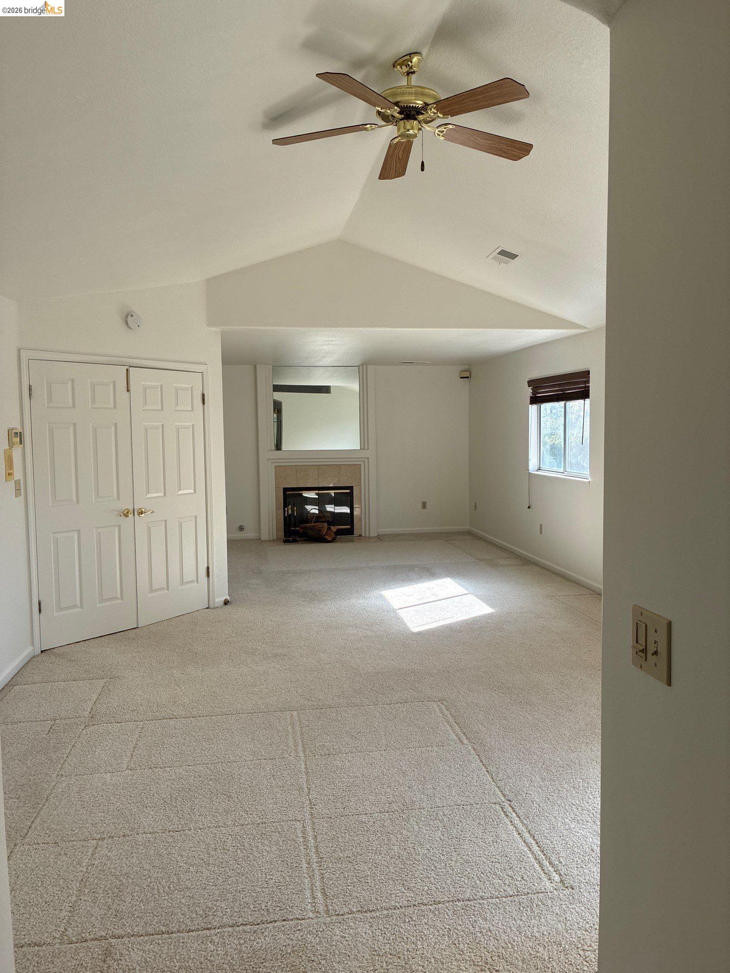 Vaulted ceiling with a ceiling fan, dual bi-fold doors, a built-in fireplace, and a window with blinds