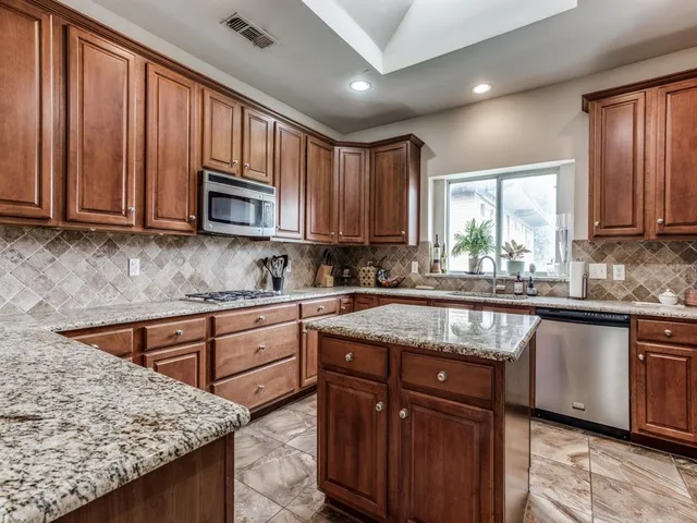 a kitchen with granite countertop wooden cabinets stainless steel appliances a window and a sink