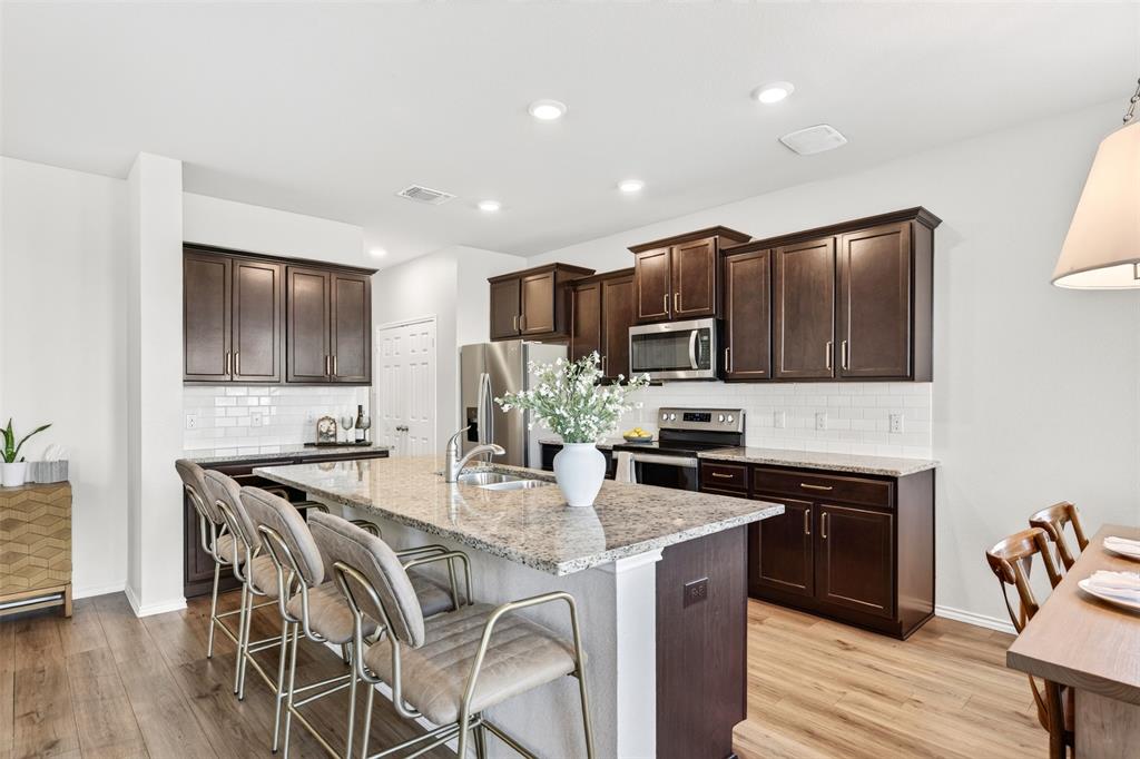 3105 Marston Road Lorena, TX 76655 - Photo 10 of 40 Spacious kitchen featuring dark wood cabinetry, stainless steel appliances, a white subway tile backsplash, and a large central island with a granite-style countertop and integrated sink