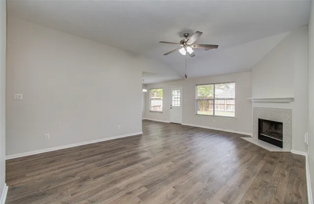 an empty room with wooden floor fireplace and windows