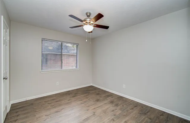 an empty room with wooden floor chandelier fan and windows