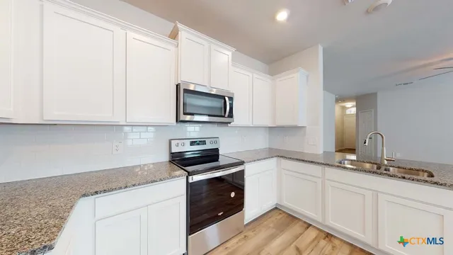 a kitchen with granite countertop white cabinets sink and stainless steel appliances