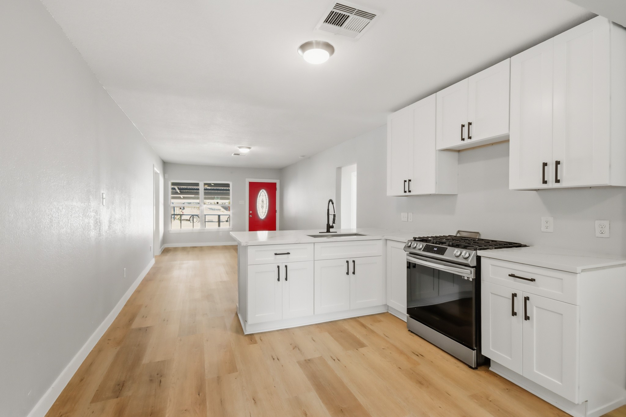 10430 Wiggins Street Houston, TX 77029 - Photo 12 of 27 This photo showcases a new modern, open-concept kitchen and living area with light laminate wood-look flooring, white cabinetry, and a stainless steel oven.