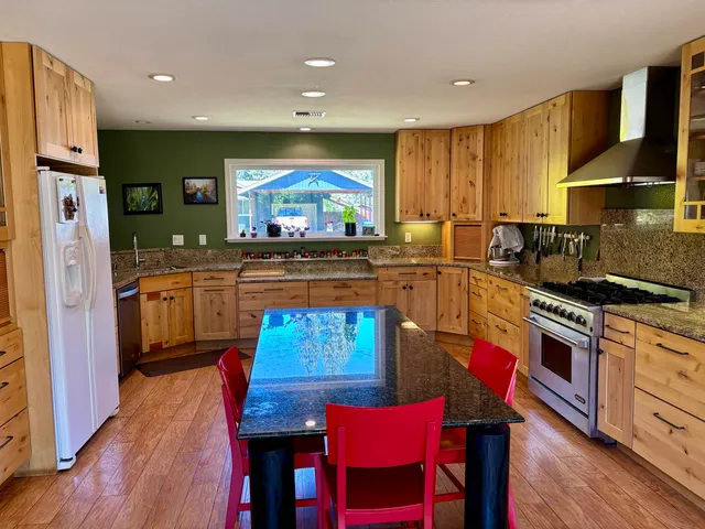 a kitchen with stainless steel appliances granite countertop wooden floors a stove a sink and a refrigerator