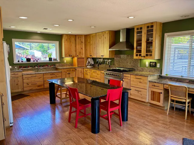 a kitchen with stainless steel appliances granite countertop a stove a refrigerator a kitchen island with chairs and wooden floor