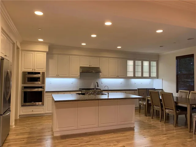 a kitchen with stainless steel appliances granite countertop a stove a sink a refrigerator and a dining table with wooden floor