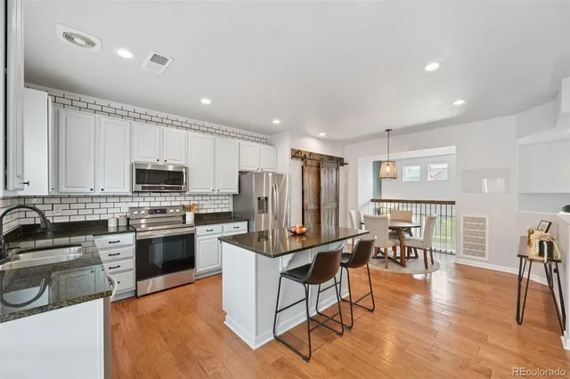 a kitchen with stainless steel appliances a stove a sink a refrigerator cabinets and a dining table with wooden floor