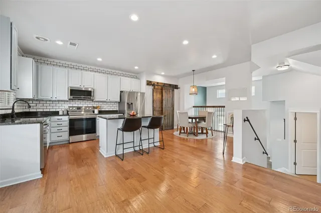 a kitchen with stainless steel appliances kitchen island granite countertop a stove top oven a sink a dining table and chairs with wooden floor