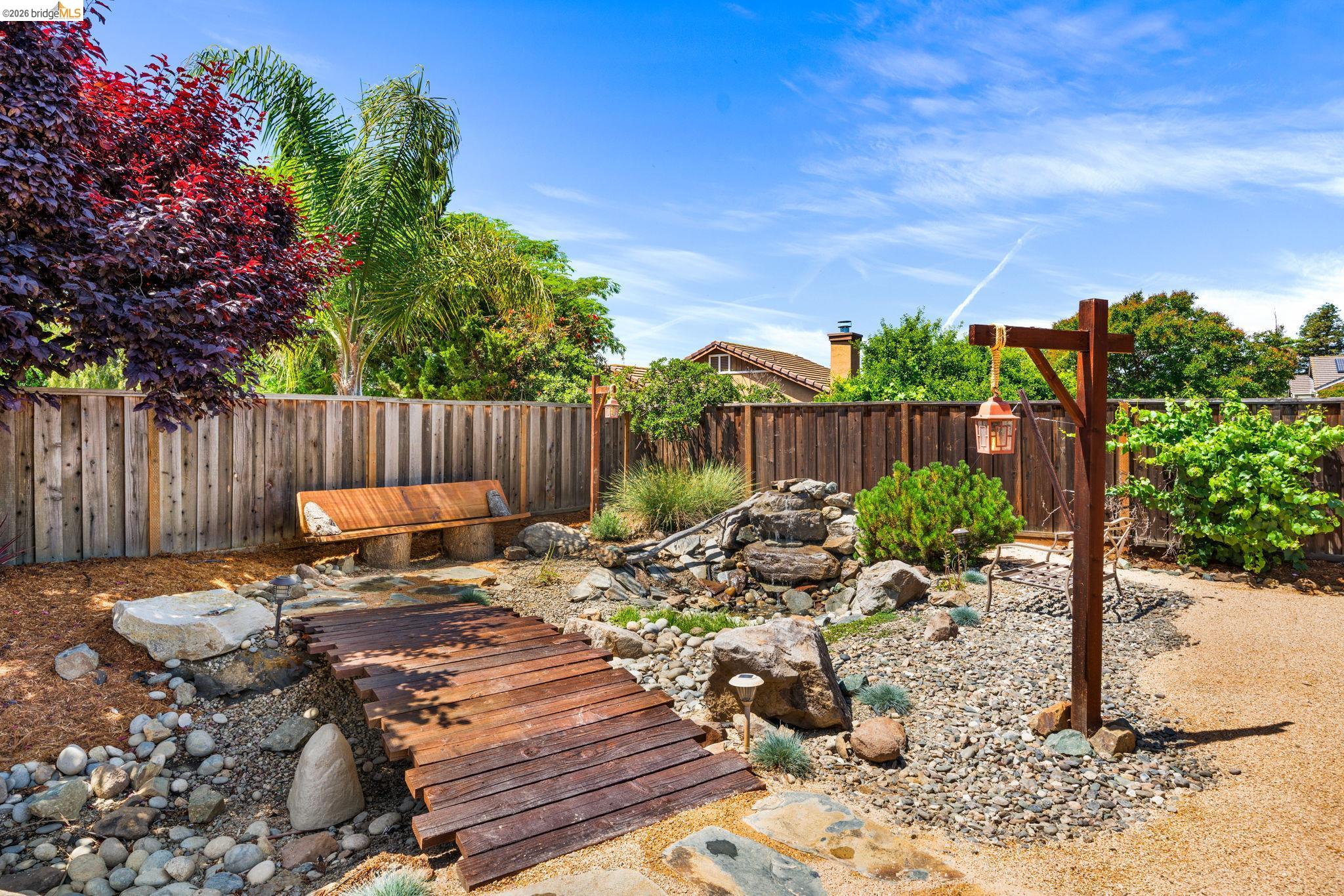 1186 El Rio Court Livermore, CA 94551 - Photo 38 of 60 Landscaped backyard featuring a tiered rock water feature, a rustic wooden bridge, and a built-in wooden bench