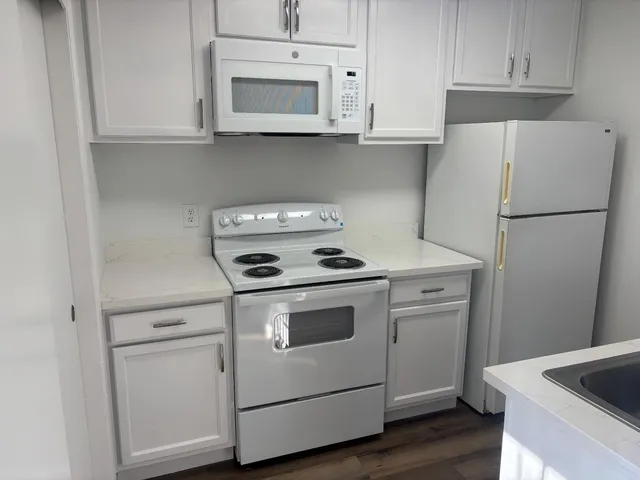 a white refrigerator freezer and a stove sitting inside of a kitchen with granite countertop white cabinets