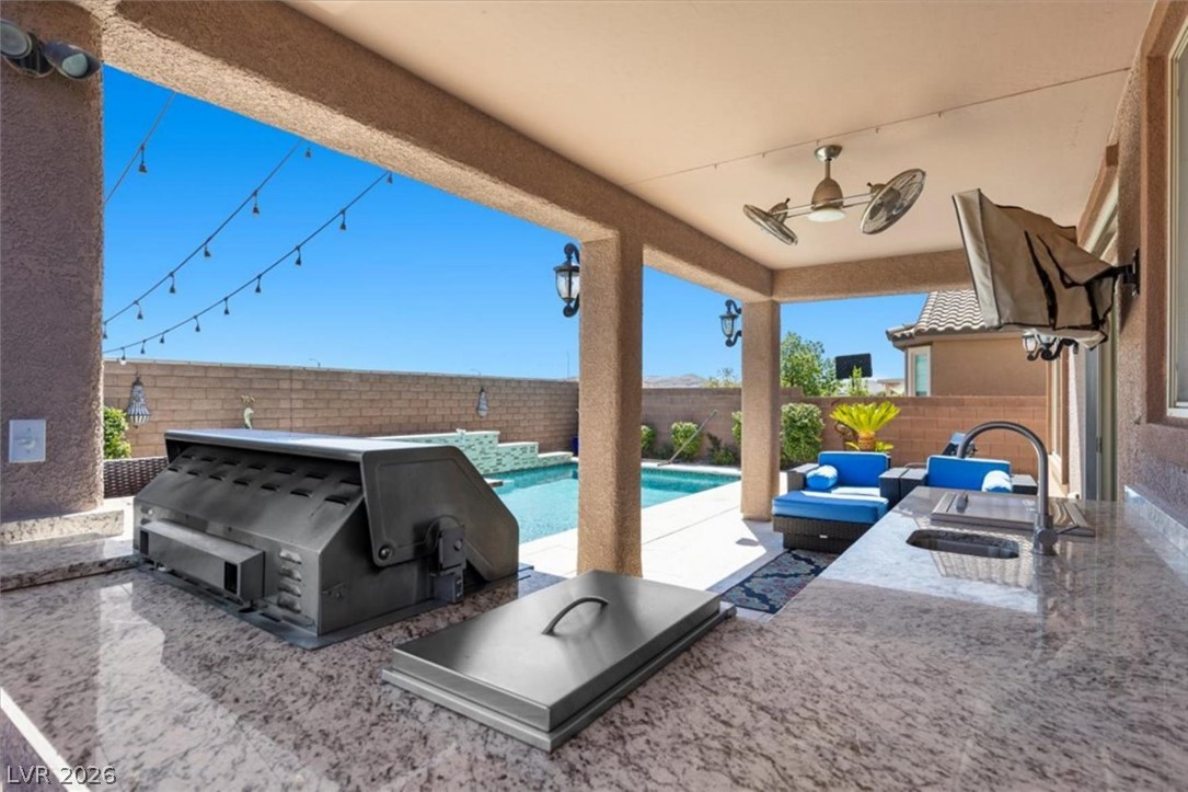 The outdoor kitchen includes a built in grill, sink, and stone counter, steps from the pool.