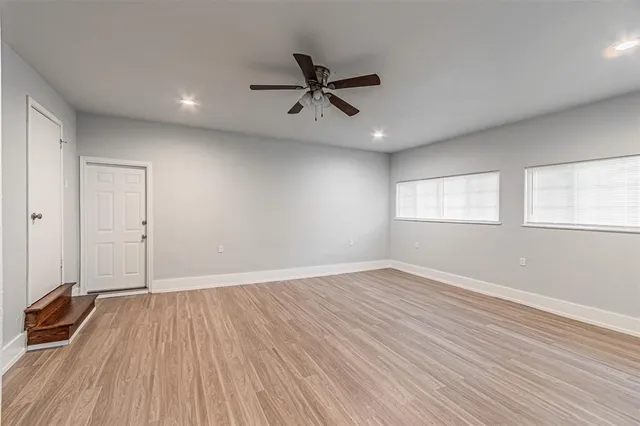 an empty room with wooden floor a ceiling fan and windows