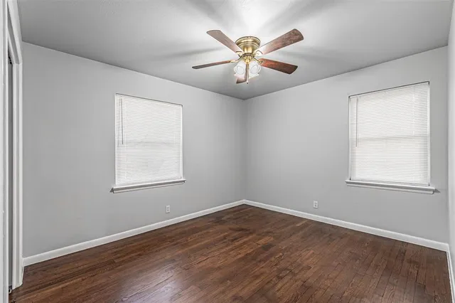 an empty room with wooden floor chandelier fan and windows