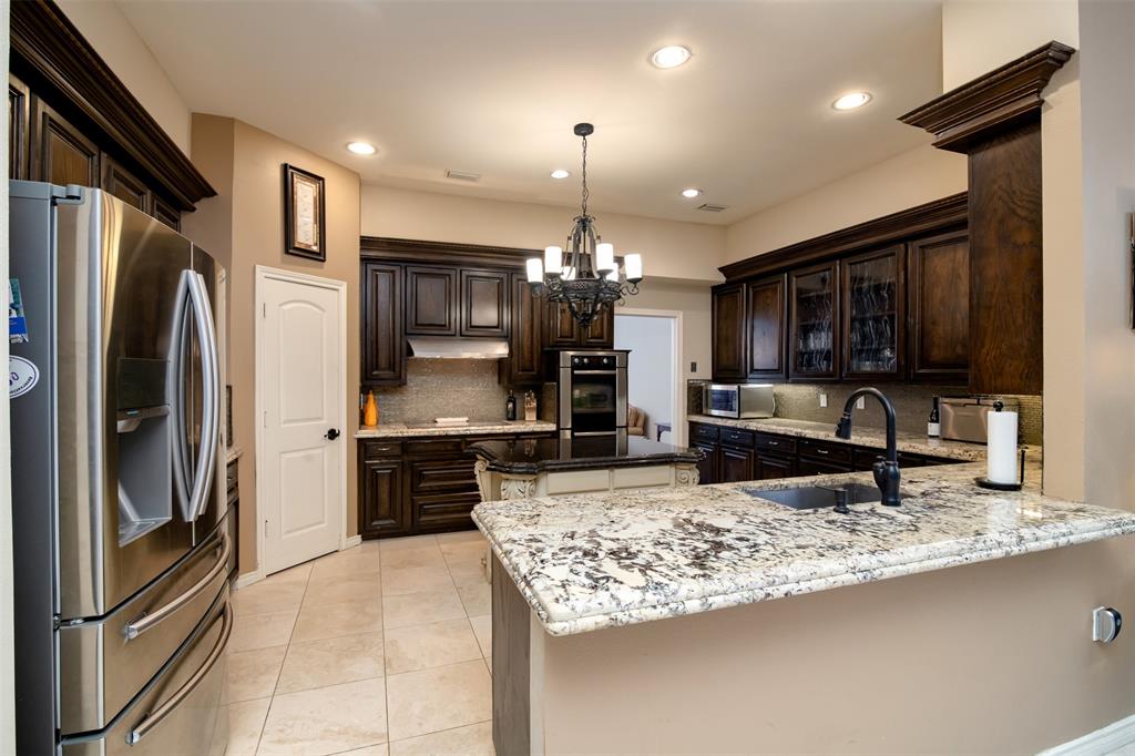 5920 Encore Drive Dallas, TX 75240 - Photo 13 of 34 Gourmet kitchen featuring dark wood cabinetry, light granite countertops, a central island with an additional sink, stainless steel appliances, and recessed lighting