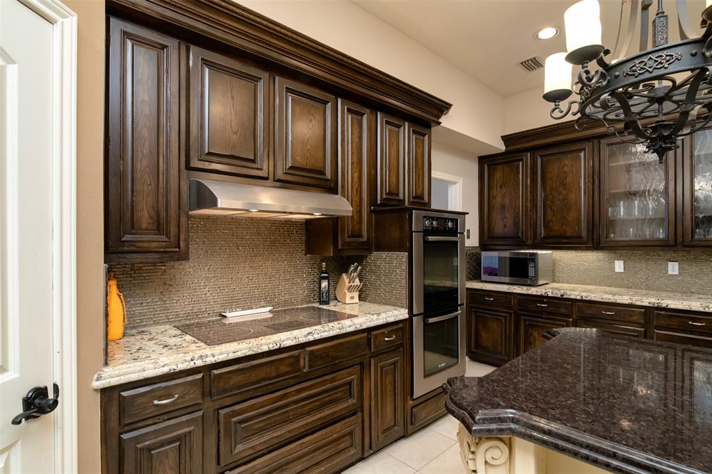 5920 Encore Drive Dallas, TX 75240 - Photo 14 of 34 Kitchen featuring dark wood cabinetry, granite countertops, a built-in oven, a stainless steel range hood, and a mosaic tile backsplash