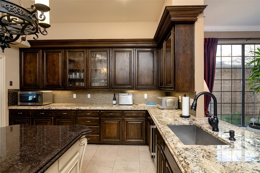 5920 Encore Drive Dallas, TX 75240 - Photo 15 of 34 Kitchen featuring dark wood cabinetry, light-toned granite countertops, and a single-basin undermount sink with a matte black gooseneck faucet