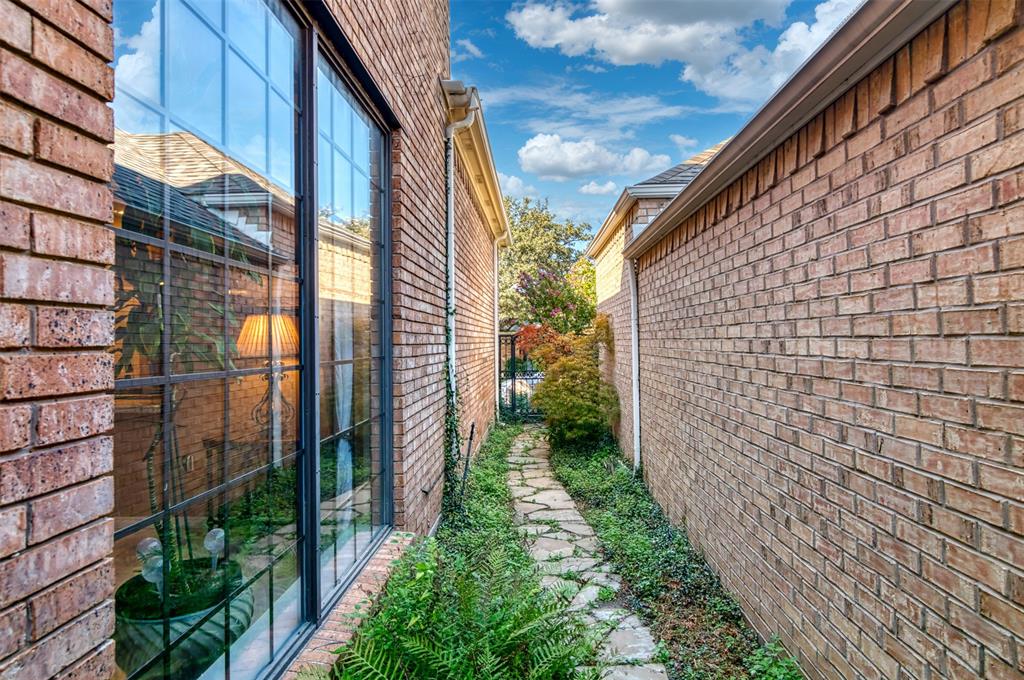 5920 Encore Drive Dallas, TX 75240 - Photo 32 of 34 Stone pathway bordered by mature plantings, featuring brick exterior walls and a large, multi-pane window