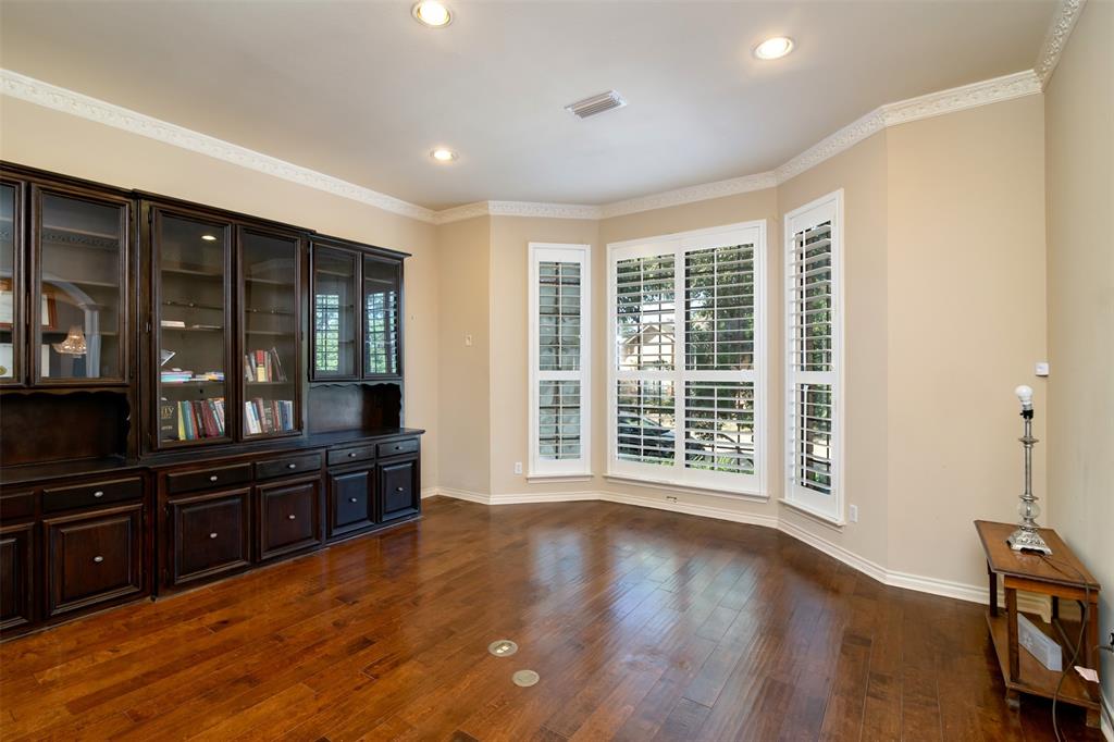5920 Encore Drive Dallas, TX 75240 - Photo 5 of 34 Room featuring wood-finish flooring, a built-in wall unit with glass-front cabinetry, multiple windows with plantation shutters, recessed lighting, and crown molding