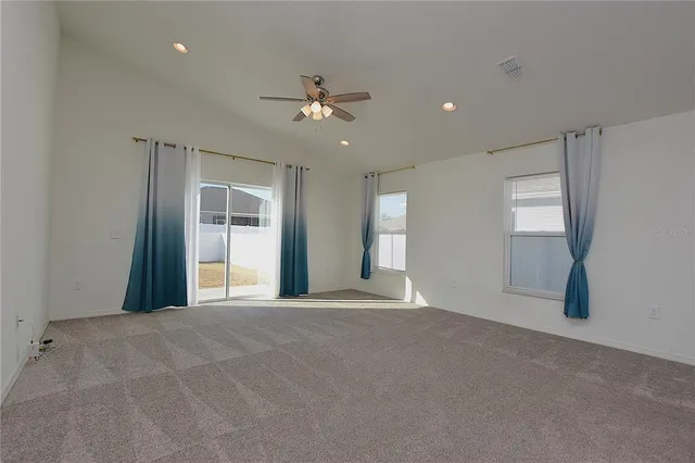 an empty room with a chandelier fan and windows