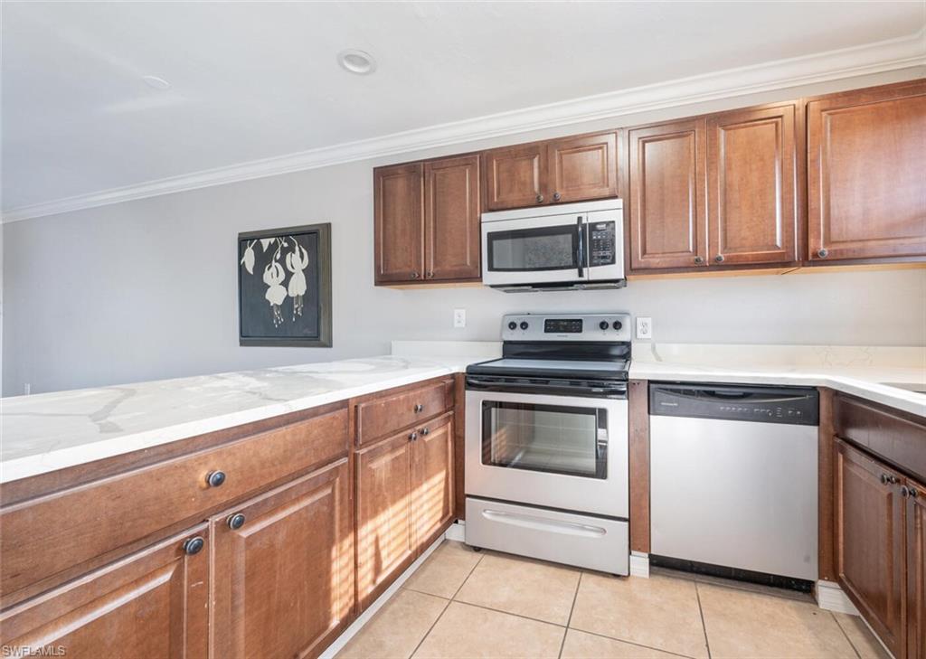 100 Forest Lakes Boulevard, Unit 305 Naples, FL 34105 - Photo 7 of 31 Kitchen with ornamental molding, light tile patterned floors, stainless steel appliances, and light stone counters