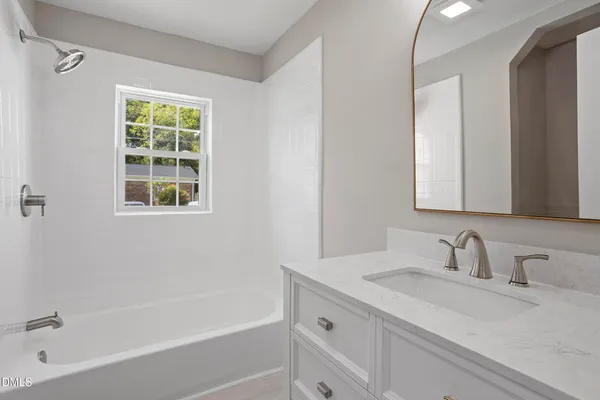 a bathroom with a granite countertop sink a mirror a bathtub and next to a window