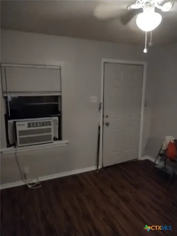 an empty room with wooden floor and way to kitchen