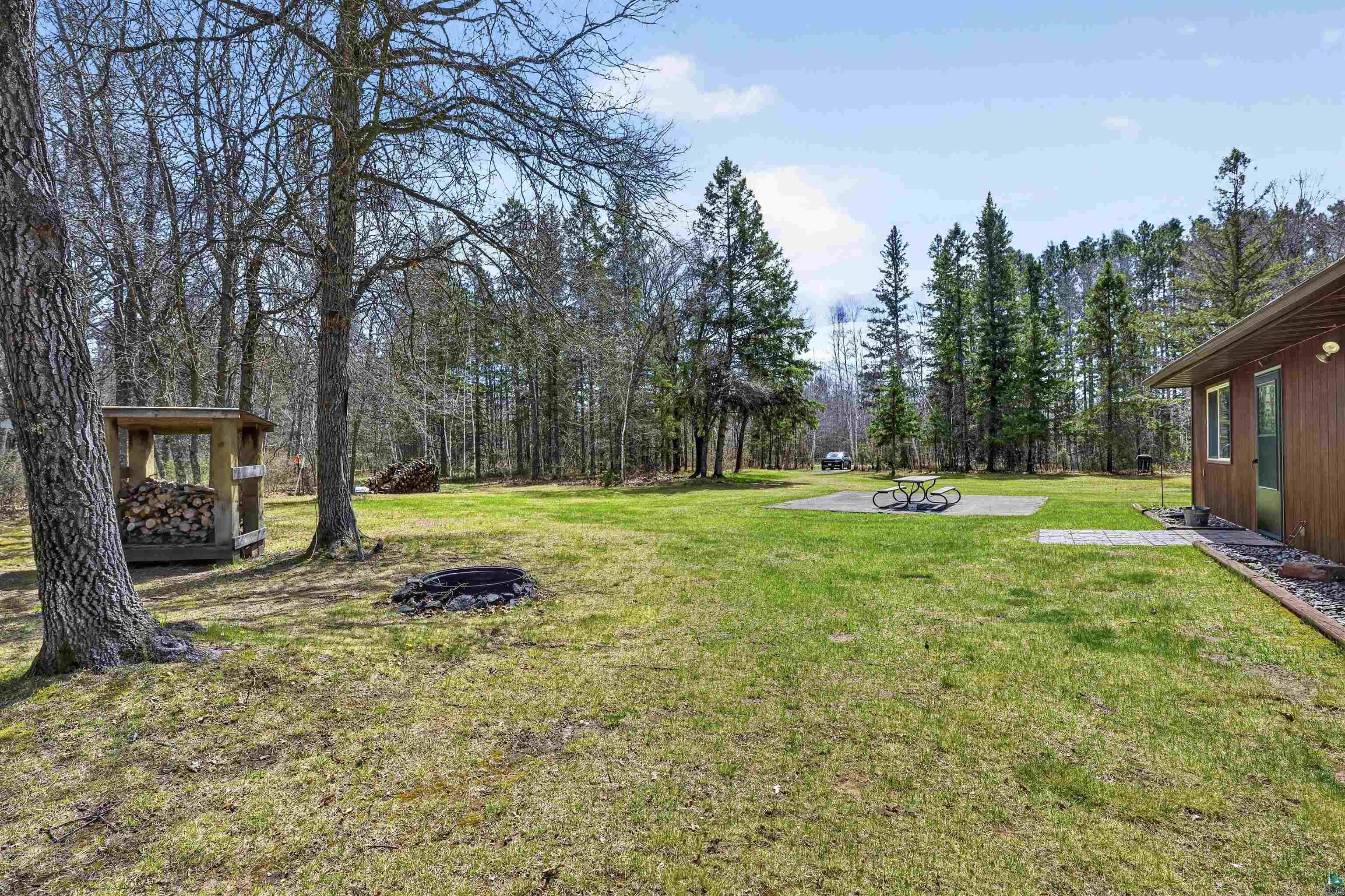 12235 East Crooked Lake Road Gordon, WI 54838 - Photo 40 of 48 Expansive grassy yard with mature trees, a wood-sided structure, a stone fire pit, and a concrete patio