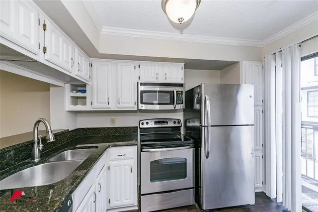 a kitchen with stainless steel appliances granite countertop a refrigerator a stove a sink and white cabinets with wooden floor