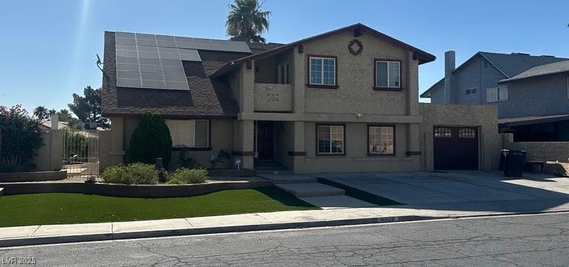 View of front of house featuring solar panels, stucco siding, and driveway