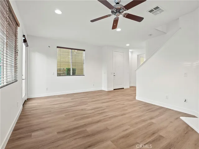 an empty room with wooden floor fan and windows