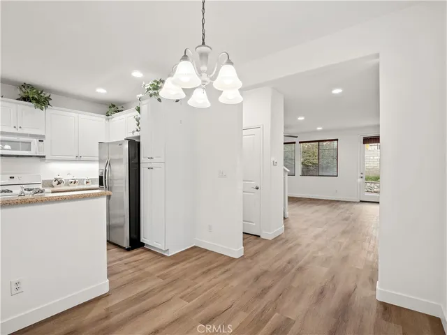 a view of a kitchen with a refrigerator a kitchen island wooden floor and a chandelier