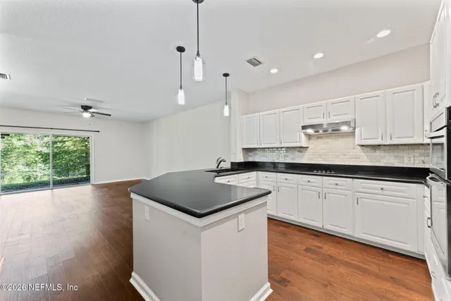 an empty room with wooden floor chandelier fan and windows