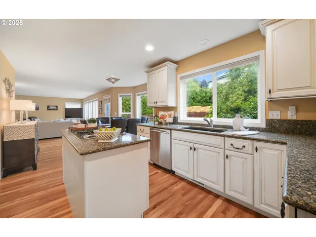 a kitchen with stainless steel appliances granite countertop a refrigerator a stove and a sink with wooden floors