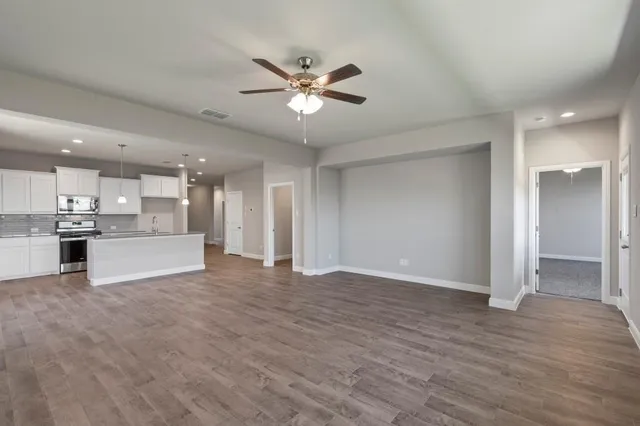 a view of an empty room with wooden floor and a kitchen
