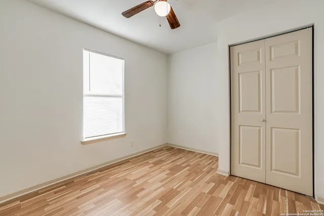 an empty room with wooden floor chandelier fan and windows
