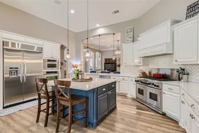 a kitchen with stainless steel appliances a stove a sink dishwasher a refrigerator and white cabinets with wooden floor