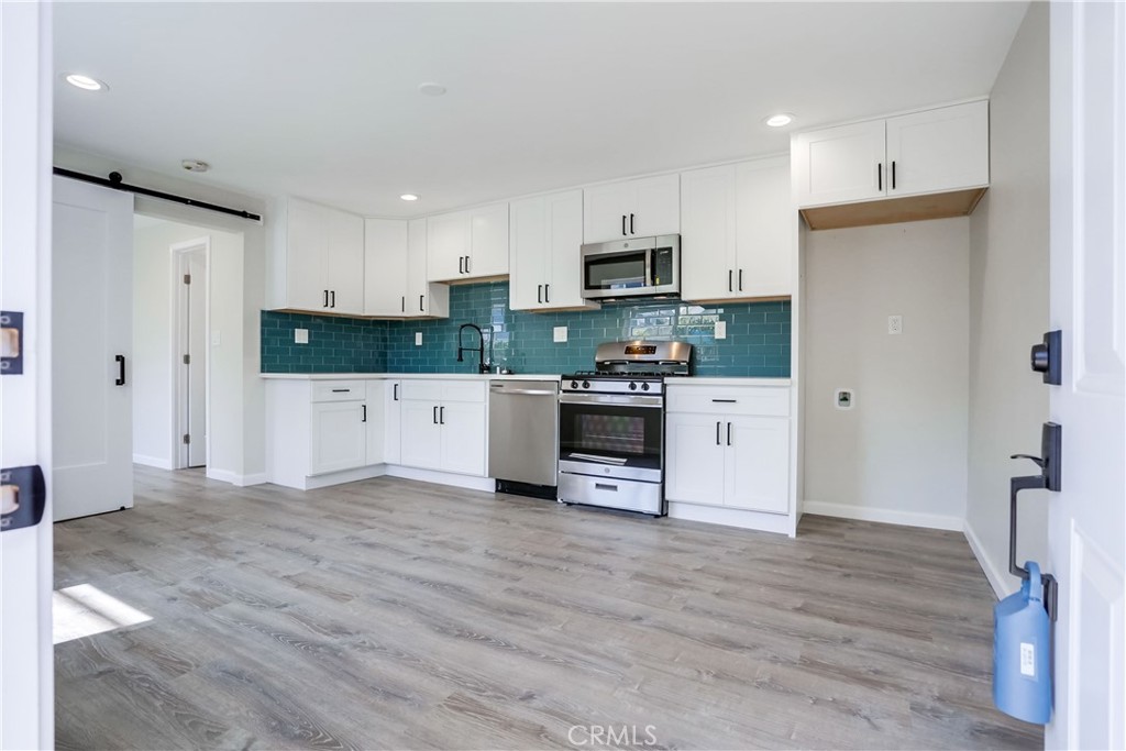 a kitchen with stainless steel appliances a stove top oven a refrigerator a sink and white cabinets with wooden floor