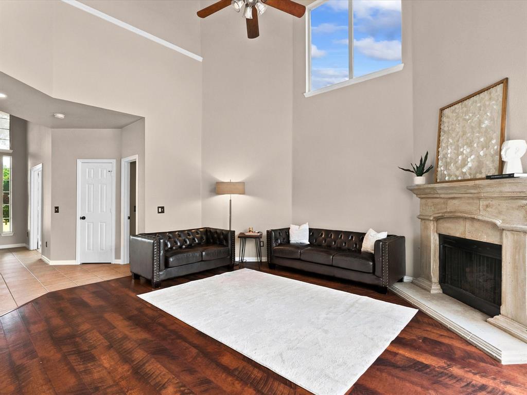 11104 Rogers Road Frisco, TX 75033 - Photo 6 of 37 Soaring ceilings with a ceiling fan, a prominent stone fireplace, and wood-finish flooring define this living area