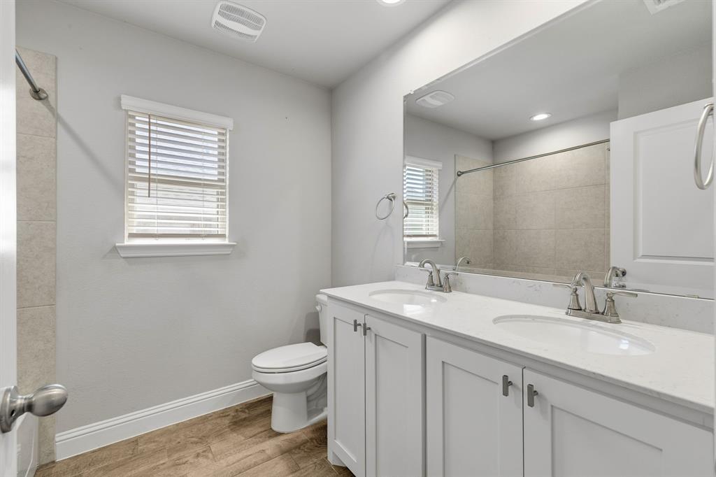915 Timber Ridge Drive Justin, TX 76247 - Photo 29 of 39 Double vanity with white cabinetry and integrated sinks, a large mirror, and wood-finish flooring