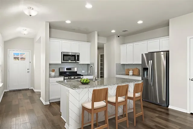 a kitchen with stainless steel appliances granite countertop a refrigerator a stove top oven a sink dishwasher and white cabinets with wooden floor