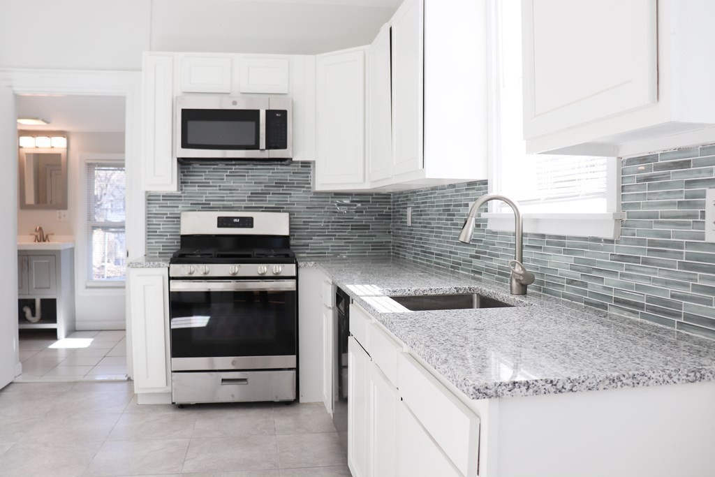 30 Woodbine Street Boston, MA 02119 - Photo 6 of 41 a kitchen with granite countertop a sink and a stove top oven with wooden floor