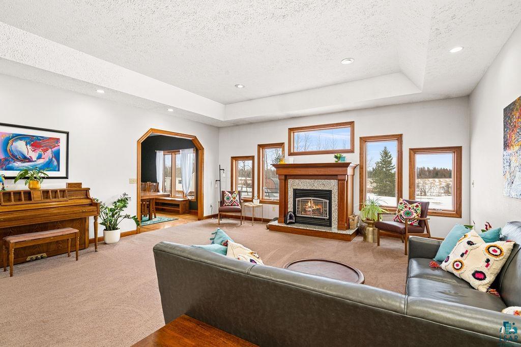 2542 Ziehl Road Carlton, MN 55718 - Photo 14 of 51 Living room featuring carpet floors, a glass covered fireplace, arched walkways, a raised ceiling, and a textured ceiling