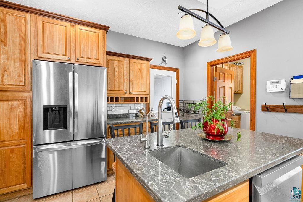 2542 Ziehl Road Carlton, MN 55718 - Photo 20 of 51 Kitchen featuring stainless steel appliances, a center island with sink, backsplash, hanging light fixtures, and light tile patterned flooring