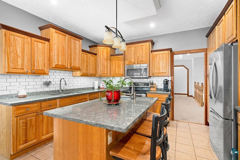 2542 Ziehl Road Carlton, MN 55718 - Photo 21 of 51 Kitchen with stainless steel appliances, dark stone counters, light tile patterned floors, a kitchen island with sink, and a kitchen breakfast bar