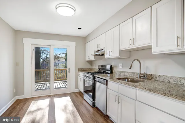 a kitchen with stainless steel appliances granite countertop a stove a sink and white cabinets with wooden floor